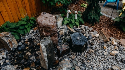 Water feature with large rocks, gravel, and greenery. Photo